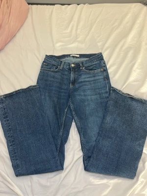 Blå bootcut jeans med låg midja - Säljer ett par klassiska blå jeans med bootcut passform och låg midja. Jeansen har fem fickor och stängs med knapp och dragkedja. Perfekta till vardagslooken och tillverkade i slitstarkt denimtyg.