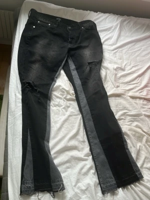 Svarta jeans med gråa detaljer från Boohoman - Unika svarta jeans från boohoman med gråa paneler längs benen och slitna detaljer vid knäna. Modellen har raka ben med råa, fransiga benslut och klassisk femficksdesign. Perfekta för dig som gillar en edgy och trendig stil.