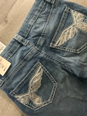 bootcut jeans - Säljer ett par blå bootcut jeans med snygga broderade detaljer på bakfickorna. Prislappen kvar. Helt oanvända. Jeansen är low waist. Från Gina tricot.  