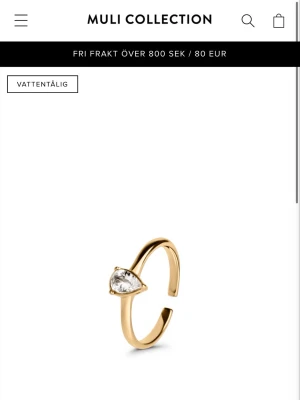 Guldfärgad ring med droppformad sten - Snygg guldfärgad ring från Muli Collection med en droppformad klar sten. Ringen har en öppen design som gör den enkel att justera och passar perfekt för dig som gillar stilrena accessoarer. Materialet är metall med en glittrande sten som ger en elegant touch.