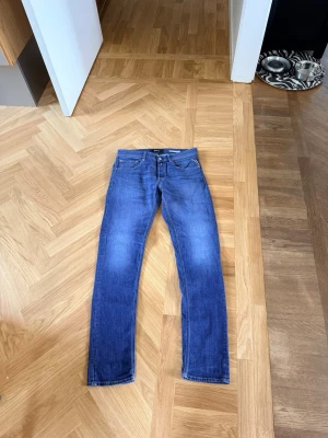 Blå raka jeans från Replay - Säljer ett par klassiska blå jeans från Replay med rak passform och fem fickor. Jeansen har snygga kontrastsömmar och metallknappar. Perfekta till vardagslooken och funkar året runt. Materialet är denim i bomull.