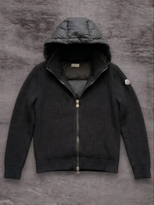Svart stickad cardigan från Moncler - Snygg svart stickad cardiganjacka från Moncler med quiltad huva och hel dragkedja. Jackan har ribbade muddar, Moncler-logga på ärmen och cool metallzipper med Moncler-emblem. Perfekt för dig som vill ha både stil och komfort.
