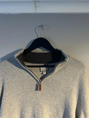 Grå halvzip-tröja  - Snygg grå stickad tröja med halv dragkedja och hög krage. Tröjan har en diskret struktur och en läderdetalj på dragkedjan. Perfekt för lager-på-lager och chill stil.