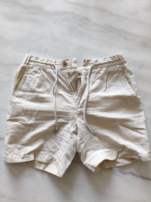 Suitsypply Beiga linneshorts - Snygga beiga shorts i linne med snörning i midjan och knappstängning. De har två sidofickor fram och två bakfickor med knapp. Perfekta för varma dagar och ger en avslappnad men stilren look.