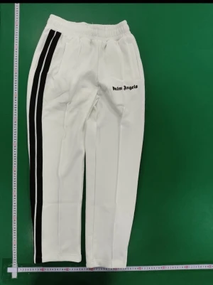 Vita mjukisbyxor Palm Angels - Snygga vita mjukisbyxor från Palm Angels med svarta dubbla ränder längs sidorna och logga tryckt på framsidan. Byxorna har resår i midjan och raka ben. Perfekta för en avslappnad och trendig stil.