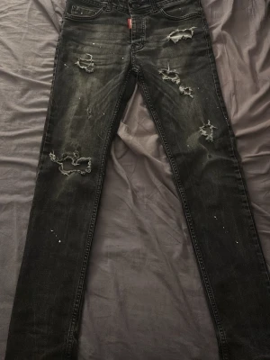 Mörkgråa jeans från Dsquared2 - Säljer ett par svarta jeans från Dsquared2 med skinny fit och coola slitningar samt färgstänk på benen. Jeansen har klassisk femficksmodell och är tillverkade i denim med stretch för extra komfort. Perfekta för dig som gillar en edgy streetstil.