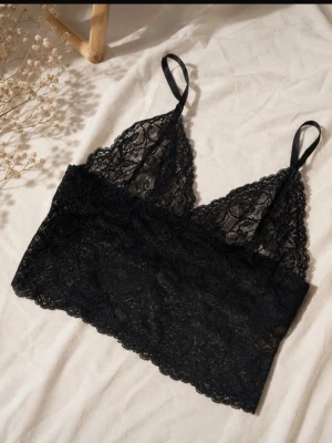 Svart spetsbralette med smala band - Snygg svart bralette i spets med justerbara smala axelband. Mjuk och stretchig modell utan bygel, perfekt för en bekväm och trendig look. Hela braletten är täckt av vacker spets med blommönster.