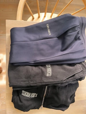 Mjukisbyxor från Les Deux - Två par mjukisbyxor från Les Deux, ett par i mörkblått och ett par i svart. Båda har resår i midjan och muddar vid bensluten. Det svarta paret har dragkedja och båda har Les Deux-loggan broderad på benet. Perfekta för en avslappnad stil.