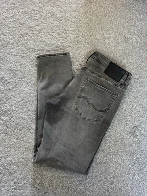 Jack & Jones jeans  - Snygga grå slim fit jeans från Jack & Jones med klassisk femficksdesign och svarta detaljer vid linningen. Jeansen har en lätt tvättad look och är tillverkade i stretchigt denim för extra komfort.