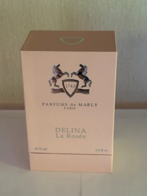 Parfums de Marly Delina La Rosée - Lyxig parfym från Parfums de Marly, Delina La Rosée, i en elegant ljusrosa kartong med silverdetaljer och klassisk logotyp. Förpackningen rymmer 75 ml Eau de Parfum och utstrålar exklusivitet och modern romantik. Perfekt för dig som gillar sofistikerade dofter.