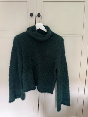 Grön fluffig polotröja Bubbleroom XS - Mysig grön stickad polotröja från Bubbleroom i storlek XS. Tröjan har en fluffig textur, lång ärm och hög polokrage. Tröjan är stor i modellen med långa armar