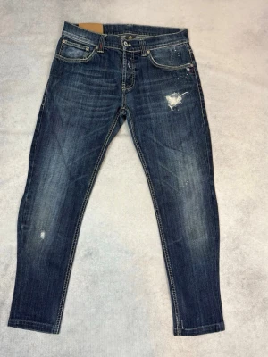 Mörkblå dondup jeans - Snygga mörkblå skinny jeans med slitningar och distressed detaljer framtill och på bakfickan. Klassisk femficksmodell med kontrastsömmar och låg midja. Perfekta för en avslappnad och trendig look. Helt nya!