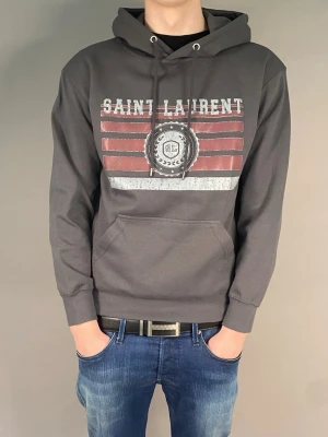 Saint Laurent Hoodie  - Skick: Mycket bra Storlek: M Färg: Grå Jag säljer en Saint Laurent tröja med en clean och enkel design som funkar till det mesta. Lätt att slänga på och matchar med både jeans eller mjukisbyxor. Passformen i storlek M sitter bra på kroppen utan att vara för tight eller för oversized, vilket syns på de två första bilderna. För referens till passformen är jag omkring 184cm lång och väger ca 73kg. Skriv vid frågor!