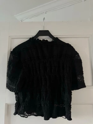 Svart spetsblus med volanger från Shein - Trendig svart blus i genombruten spets med volangdetaljer och hög hals. Blusen har korta ärmar och är väldigt luftig blus.