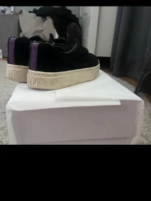 Eytys skor  - Säljer ett par svarta sneakers med lila band på hälen och tjock vit sula. Skorna har en låg profil och är tillverkade i mockaliknande material. Snygga och stilrena med coola detaljer på sulan. Perfekta för dig som vill ha något unikt i garderoben.