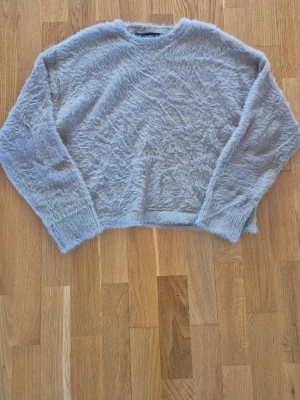 Beige fluffig tröja från Vero Moda - Mysig beige tröja från Vero Moda med fluffig och lurvig textur. Tröjan har rund halsringning och långa ärmar, perfekt för dig som gillar en chill och trendig look. Materialet är supermjukt och ger en avslappnad vibe.