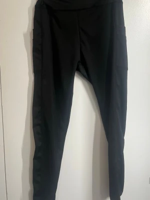 Svarta träningsbyxor med fickor - Svarta träningsbyxor med hög midja och praktiska sidofickor. Tight passform och stretchigt material som ger en bekväm känsla. Perfekta för en avslappnad och sportig stil. 