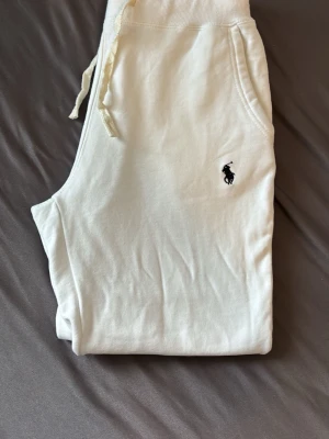 Vita mjukisbyxor från Polo Ralph Lauren - Snygga vita mjukisbyxor från Polo Ralph Lauren med klassisk logga broderad på benet. Byxorna har dragsko i midjan och sidofickor. Perfekta för en chill och avslappnad stil. Tillverkade i mjukt material för extra komfort.