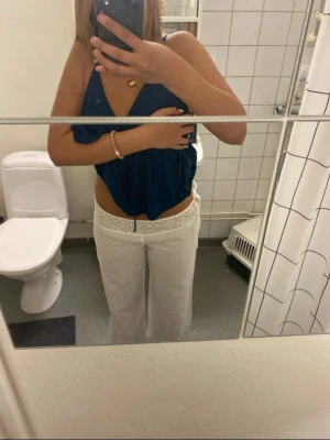 Lågmidjade linnebyxor med spetsdetalj - Snygga vita linnebyxor med bred spets i midjan och avslappnad passform. Byxorna har dragsko i midjan och är tillverkade i ett lätt och luftigt linnematerial, perfekta för en chill och trendig look.