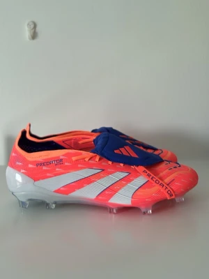 Adidas Predator fotbollsskor orange/blå - Säljer ett par Adidas Predator fotbollsskor i en riktigt fet orange färg med vita och röda detaljer samt blått snörskydd. Skorna har klassisk låg profil, mönstrad ovandel och fasta dobbar för gräsplan. Perfekta för dig som vill sticka ut på planen.