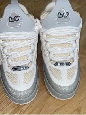 Lv skor  - Snygga Louis Vuitton sneakers i vitt och ljusgrått med meshpaneler och detaljer i läder. Skorna har tydliga LV-loggor, Box tillkommer, helt oanvända samt fina 