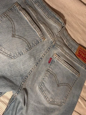 Ljusblå bootcut jeans från Levi's - Säljer ett par ljusblå Levi's jeans med klassisk femficksdesign och bootcut passform. Jeansen har den ikoniska röda Levi's-lappen på bakfickan och är tillverkade i denim. Perfekta för en avslappnad och trendig look.