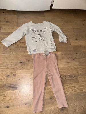 Set med tröja och leggings, H&M - Sött set från H&M med en vit långärmad tröja med texten 'Mommy is my idol' och ett par ljusrosa ribbade leggings. Perfekt för en bekväm och stilren look. Tröjan har rund halsringning och leggingsen har resår i midjan.