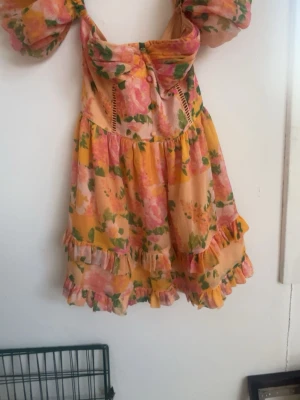 Blommig kortklänning med puffärmar - Superfin kortklänning med blommigt mönster i rosa, gul och grön. Klänningen har puffiga offshoulder-ärmar, volangdetaljer och markerad byst. 