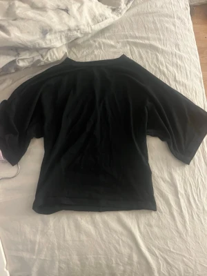 Svart tight topp med utsvängda armar 157 - Säljer en svart topp från 157. Modellen har en loose passform med korta ärmar och rund halsringning. Perfekt för dig som gillar en enkel men ändå lyxig look.