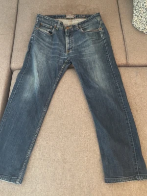 Blå jeans med slitningar - Klassiska blå jeans med raka ben och snygga slitningar framtill. Jeansen har fem fickor och kontrastsömmar. Perfekta för en avslappnad och trendig look. Materialet är denim i bomull. Märket: Dressmann. Har inte använt den många gånger, är ganska ny för mig. Men allt se bra ut och verkar perfekt.