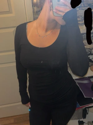Svart långärmad topp i bomull - En basic svart långärmad topp med rund halsringning. Tillverkad i mjuk bomull som sitter tight och framhäver figuren. Perfekt att styla med jeans eller kjol för en clean look.