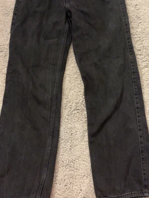 Svarta raka jeans i denim - Säljer ett par svarta jeans med rak passform och klassisk femficksdesign. Jeansen är tillverkade i denim och har en enkel, stilren look som passar till det mesta. Perfekta för dig som gillar en avslappnad och tidlös stil.