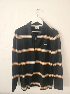 Randig långärmad skjorta Lacoste - Snygg långärmad skjorta från Lacoste med svarta, vita och bruna horisontella ränder. Klassisk krage och knappar framtill. Perfekt för en avslappnad och stilren look.