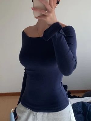 Mörkblå offshoulder topp - Snygg mörkblå offshoulder topp med lång ärm och figurnära passform. Toppen har en stilren och enkel design som passar perfekt till jeans eller kjol. Mjuk och stretchig kvalitet för en bekväm känsla.