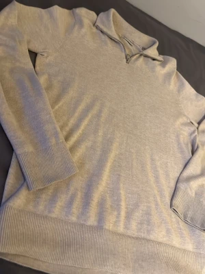 Beige stickad tröja med halvzip - Snygg beige stickad tröja från Jack & Jones med halvzip och ståkrage. Tröjan har långa ärmar, ribbade muddar och nederkant. Perfekt för lager-på-lager och enkel att matcha med jeans eller chinos.