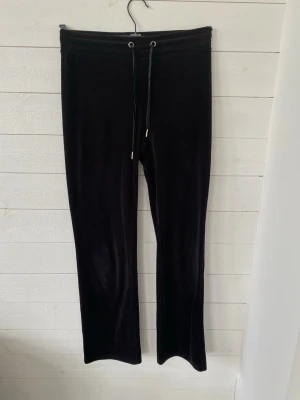 Svarta mjukisbyxor från Gina Tricot - Svarta mjukisbyxor från Gina Tricot i mjukt velourmaterial. Byxorna har raka ben, resår i midjan och dragsko med metalländar. Perfekta för en chill och avslappnad stil.