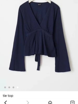 Mörkblå gina tröja med knyt - Snygg mörkblå omlottopp från Gina Tricot med långa ärmar och knyt i midjan. Toppen har v-ringad hals och är tillverkad i ett mjukt, lätt strukturerat material. Perfekt för dig som gillar en enkel men trendig look.