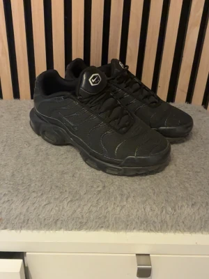 Svarta Nike TN skor  - Säljer mina svarta Nike TN air Max skor då det är för små och inte min stil men i väldigt fint skick och har lite smuts som kan gå bort, finns samt två saker som har gått av på skon som visas i de sista bilderna men går nog att limma på!                        Pris kan diskuteras vid snabb affär! Sko lådan kommer också med!