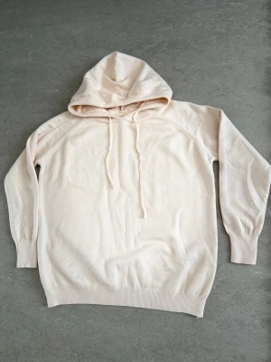 Orange/beige hoodie med huva - En stilren ljusbeige hoodie med huva och dragsko. Hoodien har långa ärmar, ribbade muddar vid ärmslut och nederkant samt en relaxed passform. Perfekt för en chill och avslappnad look. Materialet känns mjukt och bekvämt mot huden.