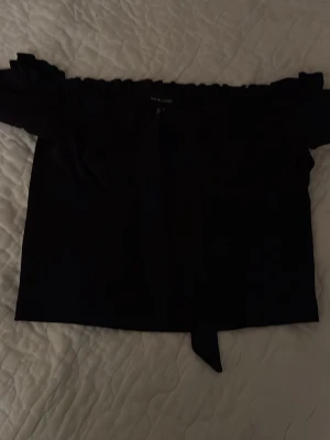 Svart offshoulder topp från New Look - Säljer en svart offshoulder topp från New Look. Toppen har en rak passform och elastisk kant upptill som håller den på plats. Perfekt till jeans eller kjol för en trendig look.