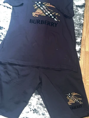 Svart set från Burberry med logga - Säljer ett svart set från Burberry med klassisk riddarlogga och Burberry-tryck på både tröja och shorts. Setet är gjort i mjukt material och har en avslappnad passform. Perfekt för dig som gillar stilrena och exklusiva detaljer. Går inte billigare än 499