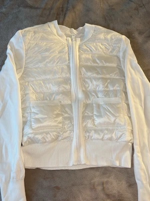 Vit quiltad cardigan från Gina Tricot - Köptes förra året hängt i garderoben med prislappen användes 1 gång men kommer tyvärr inte till användning. Passar mig som är 170 cm, passar mig som har storleken ”S” i kläder. Sitter fint och längst med kroppen. Stilren vit cardiganjacka från Gina Tricot med quiltad front och två fickor. Jackan har dragkedja framtill, ribbade muddar och slätstickade ärmar. 