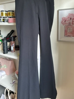 Svarta utsvängda kostymbyxor RYVLS - Säljer ett par svarta kostymbyxor från RYVLS med utsvängda ben och låg till midwaist . Byxorna har en stilren look och är tillverkade i ett mjukt, följsamt material som ger en snygg siluett. Perfekta för dig som gillar trendiga och bekväma byxor.