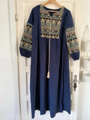  långklänning från SHEIN - Marinblå långklänning från SHEIN med broderade detaljer i vitt och vinrött på bröst och ärmar. Klänningen har lång ärm, lös passform och dekorativ snörning framtill. Perfekt för dig som gillar boho-vibbar och unika mönster.