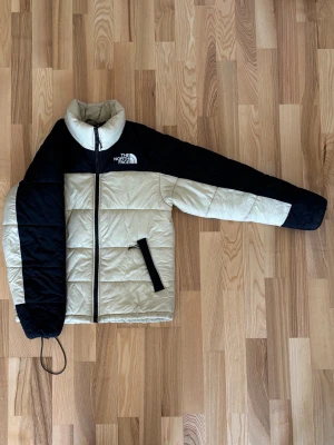 Beige och svart dunjacka The North Face - Säljer en beige och svart dunjacka från The North Face med broderad logga på bröstet. Jackan har hög krage, dragkedja framtill och två snedställda fickor. Klassisk boxig passform och quiltad design. Perfekt för kalla vinterdagar. Den är storlek M men själv har jag S och passar bra men luftig, så den passar till båda storlekar! 