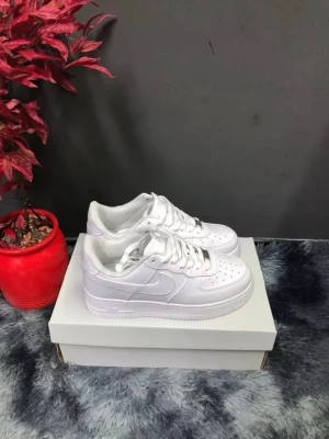 Nike Air Force 1 vita sneakers - Ändast testade! Klassiska helvita Nike Air Force 1 sneakers i lågt utförande. Skorna har en stilren design med perforerad tå, vita skosnören och den ikoniska swoosh-loggan på sidan. Tillverkade i läder med gummisula för bra grepp. Perfekta för dig som gillar en clean och tidlös look.