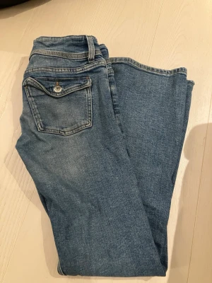 Blåa jeans från Gina Tricot - Ett par klassiska blå jeans från Gina Tricot i storlek 152. Jeansen har en bakficka med knappdetalj och är tillverkade i mjukt denimtyg. Perfekta för dig som gillar en enkel och tidlös stil.
