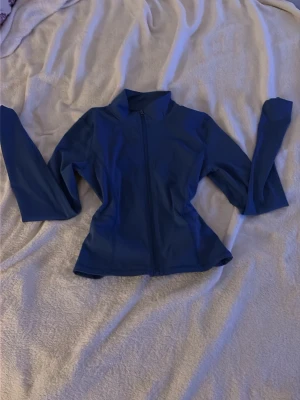 Blå ziptröja med hög krage (tränings tröja) - Snygg blå ziptröja med hög krage och långa ärmar. Tröjan har en figurnära passform och dragkedja framtill. Perfekt för en sportig och avslappnad stil. Köpt länge sen vet inte var ifrån. Liten i storlek men är stretch