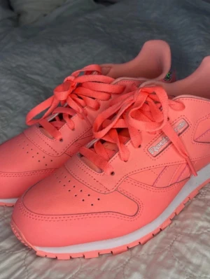 Korallrosa Reebok sneakers - Andvända en gång !Snygga korallrosa sneakers från Reebok med klassisk design och lågt skaft. Skorna har matchande skosnören, perforerade detaljer på tån och vit sula med rosa inslag. Tillverkade i syntetmaterial och textil för en fräsch look.