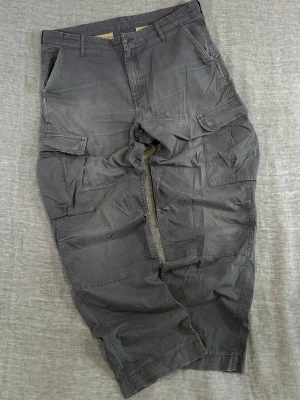 Carhartt WIP Ripstop Cargo Pants Tactical Utility fit Graphite Grey 34x32 - carhartt wip cargo pants in ripstop cotton with that clean grid texture. faded graphite grey tone with a relaxed utility fit. classic multi pocket cargo layout + articulated knees. perfect everyday streetwear piece.  measurements (flat): waist 46cm rise 30cm thigh 34cm knee 28.5cm leg opening 22cm length 109cm  condition: worn with small hole on left hip, light wear on hips/inner thigh and missing back pocket snap (all shown)